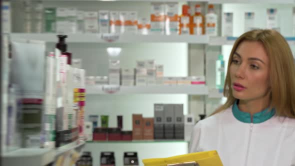 Young Female Pharmacist Walking in the Drugstore, Checking Products in a List