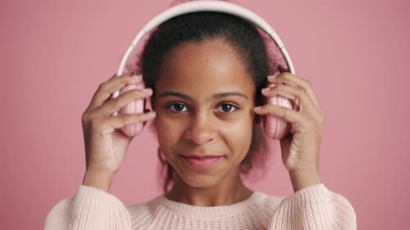 Cheerful African little girl listening music in headphones