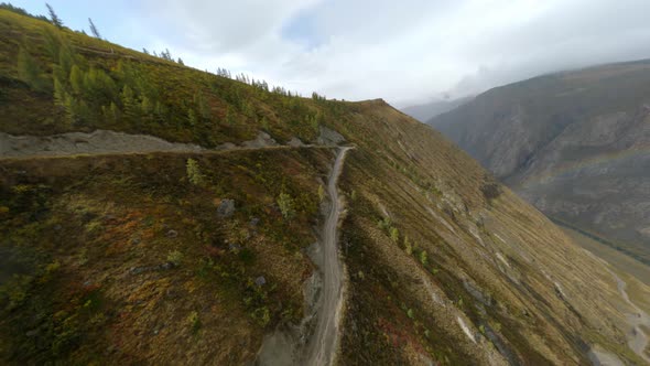 Black Automobile Riding on Dangerous Path with Rainbow Over Valley Scenery