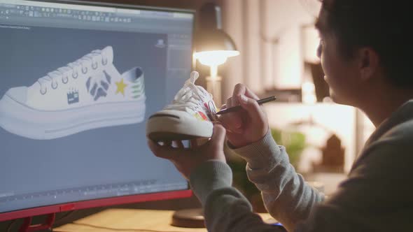 Asian Male Footwear Designer Putting Coloured Unique Patterns On Sneakers While Designing Shoe