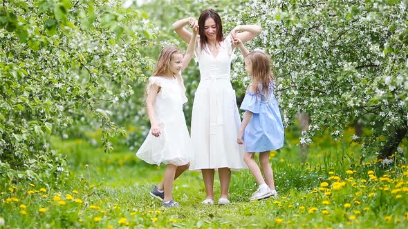 Adorable Little Girls with Young Mother in Blooming Garden on Beautiful Spring Day Having Fun