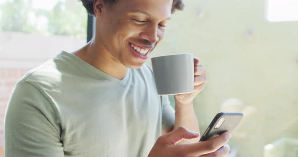African american man using smartphone and drinking coffee at home