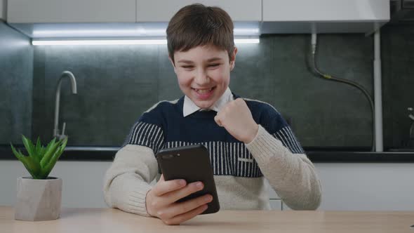 Happy 13 Years Old Boy Reading Great News Online on His Smartphone While Sitting at Home