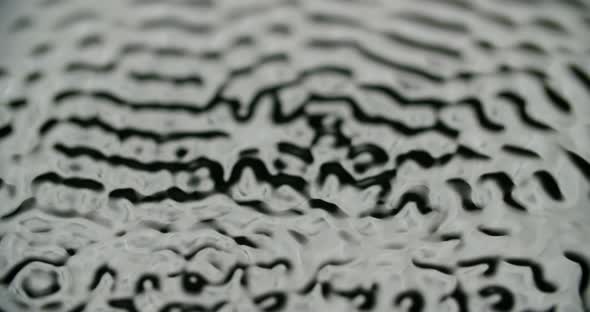 Macro shot of water surface vibrating to frequency. Water forming waves and ripples.