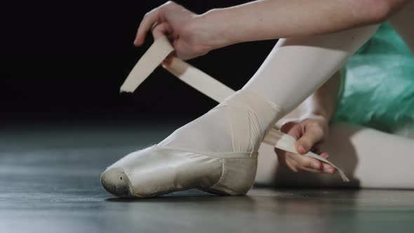 Unrecognizable Girl Ballerina Dancer Sits on Floor in Dance Class on Stage Puts on Pointe Shoes Ties