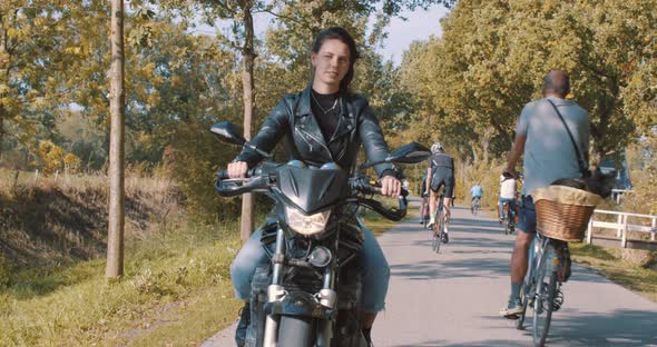 Woman riding a motorcycle in fall in nature, wearing leather jacket driving On road passing cyclists