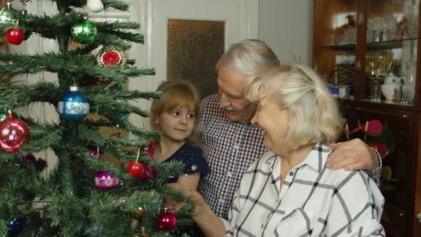 Girl Kid with Senior Grandma Grandpa Decorating Artificial Christmas Tree with Ornaments and Toys