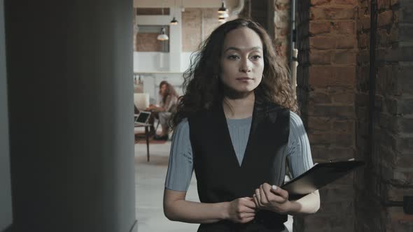 Mixed-Race Businesswoman with Clipboard Walking along Loft Corridor