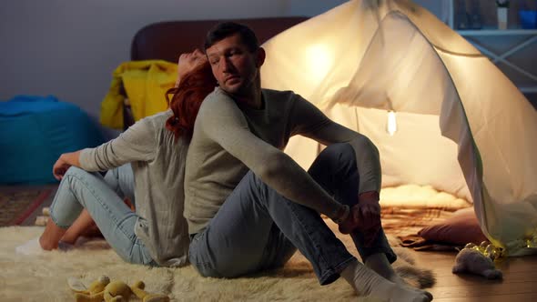 Wide Shot Relaxed Happy Husband Sitting Back to Back with Wife at Tent in Living Room Smiling