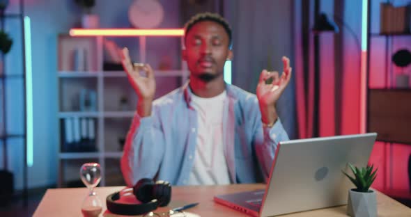 African American Sitting at His Workplace at Home in the Evening and Meditating