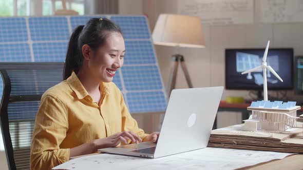 Smile Asian Woman Typing On A Laptop Next To The Model Of A Small House With Solar Panel