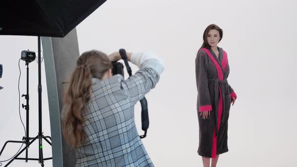 Back View of Woman Using Photo Camera to Shoot Female Model in Pink Bathrobe During Photoshoot in
