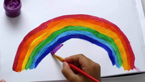 The girl draws a rainbow on paper with multicolored paints. Drawing with the eyes of a child.