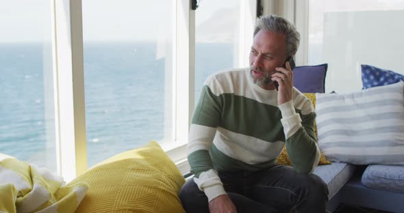 Happy caucasian mature man looking through the window and using smartphone