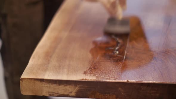 A craftsman is finishing a custom hand made natural wood table top with a coat of varnish in his woo