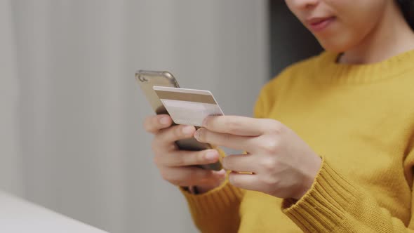 Woman holding credit card and using smartphone at home.