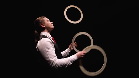 Camera Rotates Around Concentrated Man Juggling White Rings Then Puts Them Around His Neck