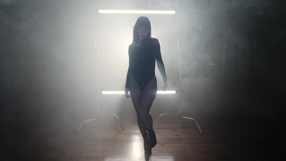 Beautiful Dancer Woman Walking Through Smoke Between Long Lamps and Looks Seductively Into Camera