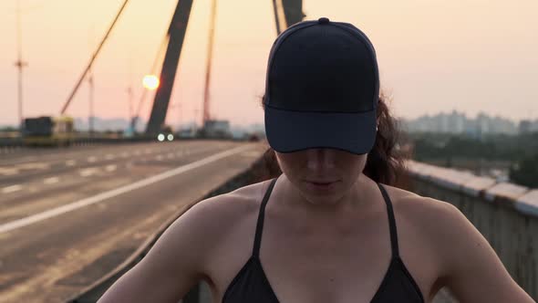 Young Motivated Girl is Preparing to Run on City Bridge During Sunset