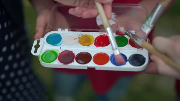 Closeup Painting Palette with Children Hands Coloring Brushes in Slow Motion