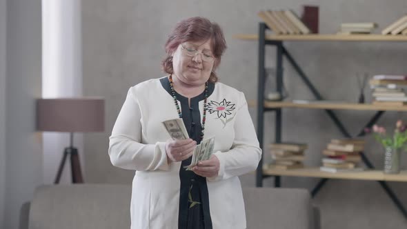 Happy Wealthy Senior Woman in Eyeglasses Counting Money Showing Cash Looking at Camera