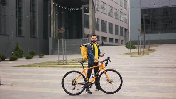 The Food Delivery Guy is Standing and Holding the Smartphone