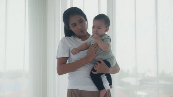 Young asian mother holding little baby girl and walking together in the bedroom at home.