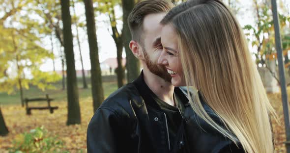 Happy Man Whispers in His Laughing Girlfriend's Ear While They Stand in Park