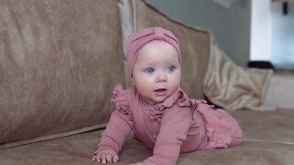 A Baby Girl with Blond Hair and Blue Eyes in Pink Clothes Lies on Her Tummy and Swings in Different