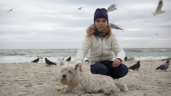 Portrait of Curly Little Girl Squatting on Sand Close to Her Puppy Stroking It Taking Pleasure Being