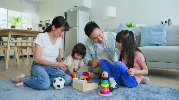 Asian happy family sit on floor, play with little kid daughter together in living room in house.