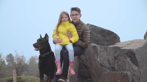 Teenage Caucasian Brother in Eyeglasses Holding His Younger Sister on Hands