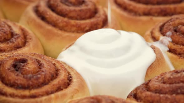 pouring fluffy frosting on Freshly baked cinnamon rolls or Cinnabon close up.