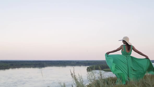 Young Woman in a Green Dress Posing on the Background of a Beautiful Landscape