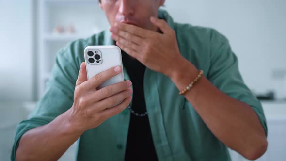 Closeup of Shocked Young Man Using Smartphone Loses Dissatisfied with Bad News at Home