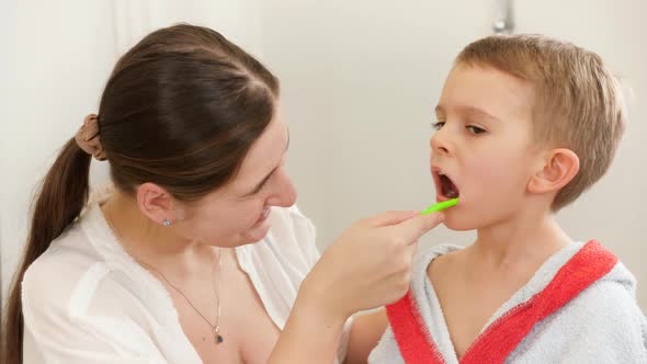 Young Smiling Mother Brushing and Cleaning Teeth of Her Little Son with Tothbrush