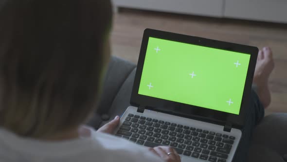 Woman at Home Sitting on a Couch Corks on a Laptop Computer with Green Mock-up Screen. Girl Using