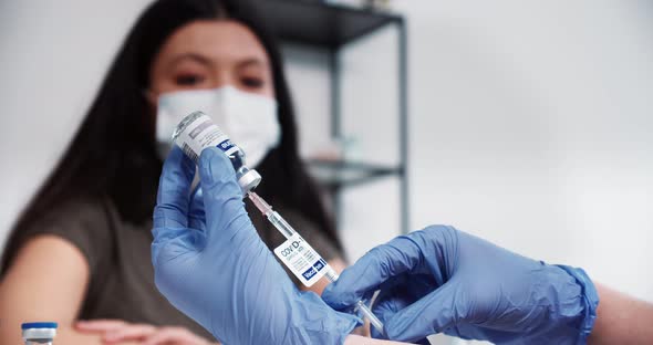 Closeup on Doctor Hands in Blue Gloves Using Vaccine Syringe and Flask to Give Injection Shot to