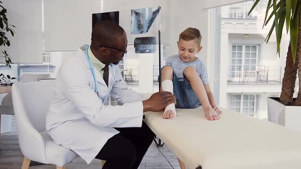 Male Doctor Bandaging Leg of Cute Boy