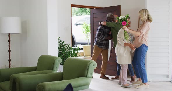 Two diverse senior couples hugging and greeting each other at home