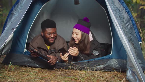 Diverse Travelers with Gadgets Resting in Camp Tent