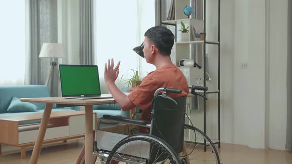 Young Asian Boy Sitting In A Wheelchair While Video Call On Laptop With Green Screen At Home