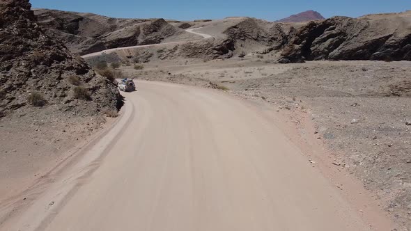 Drone footage of the rocky terrain region with dusty roads and cars driving