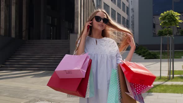 Girl Walking From Shopping Mall with Shopping Bags and Talking on Mobile Phone About Purchases