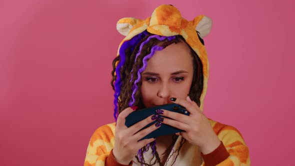 A Handsome White Woman with Dreadlocks and in Kigurumi is Playing an Online Game on a Smartphone on