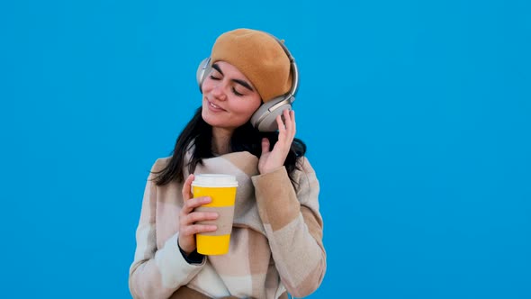 Woman with Headphones and Paper Cup Looking at Camera