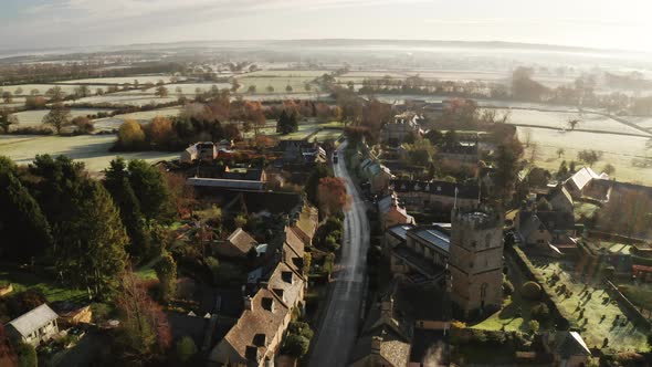 Aerial drone video of a Cotswolds Village, English countryside fields and scenery with houses, prope