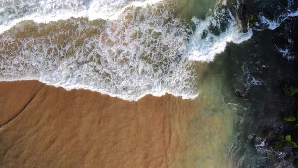 waves breaking at black rocks in Geriba Beach in Buzios, Brazil, Aerial top down view