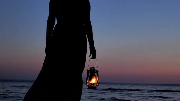Lonely Woman in Dress Holding Kerosene Lantern and Looking at Sunset Sky Background