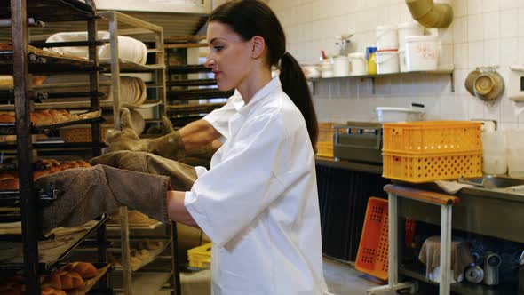 Female baker removing baked michetta from baking trolley